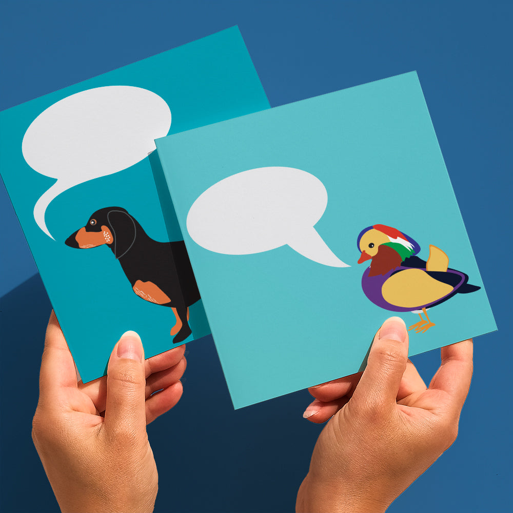 Colourful greetings card with mandarin duck illustration and speech bubble to add your own message  shown half in hands with a second card with dachshund illustration held behind 