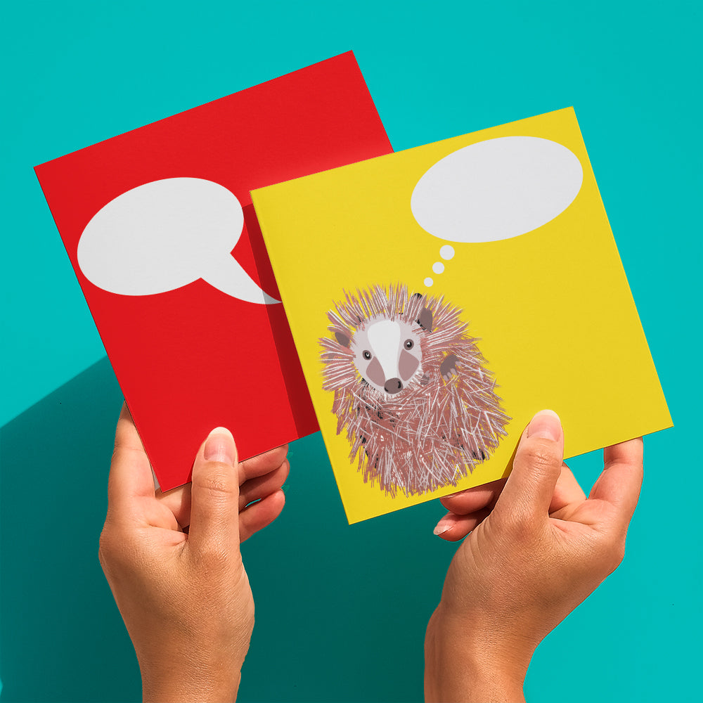 Bright yellow greetings card with hedgehog illustration and  thought bubble to add your own message shown being held in hand with a second red card behind 